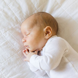 Newborn baby asleep with hands by his face